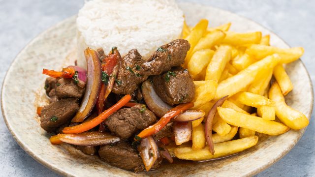 Closeup of roasted meat with sauce, vegetables and fries in a plate on the table